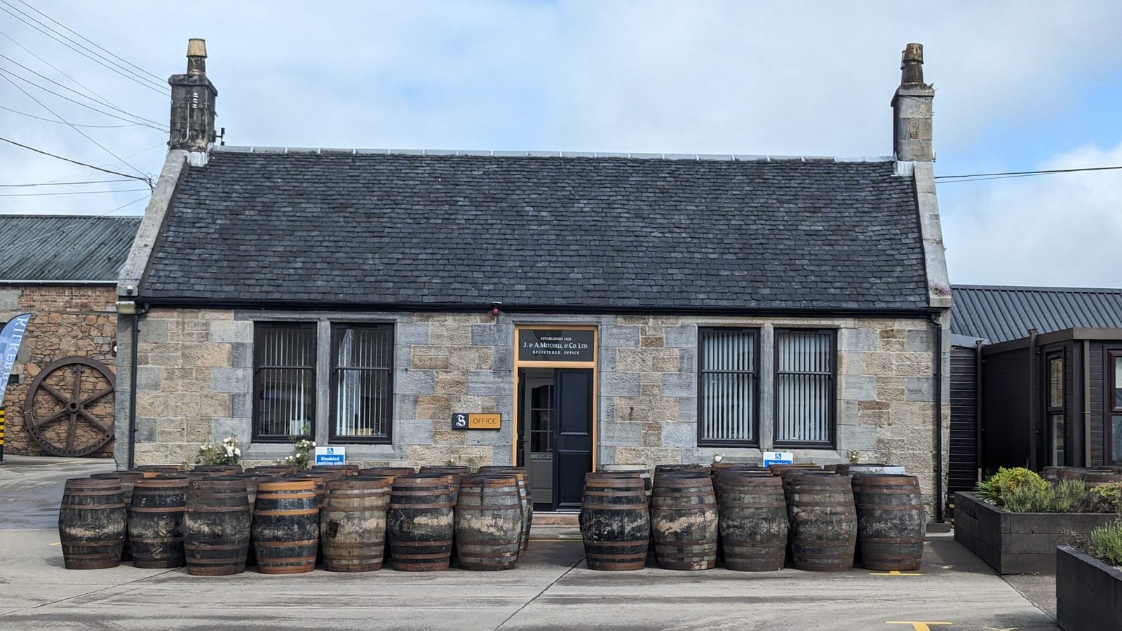 A stone Springbank distillery building in Campbeltown with whisky casks stacked outside.