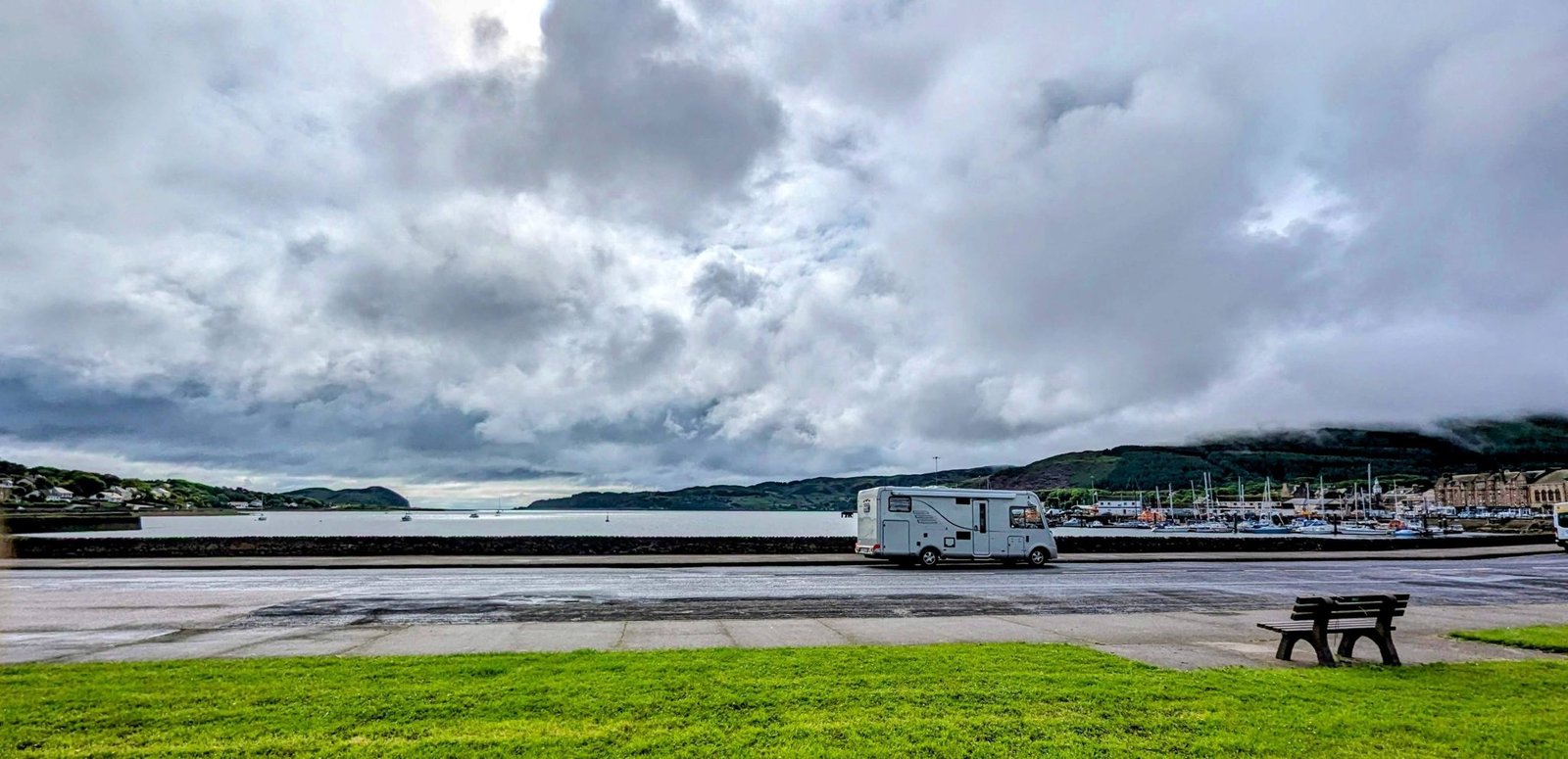 A motorhome parked on grass at Kinloch Park in central Campbeltown, with a picnic bench and the harbour beyond.