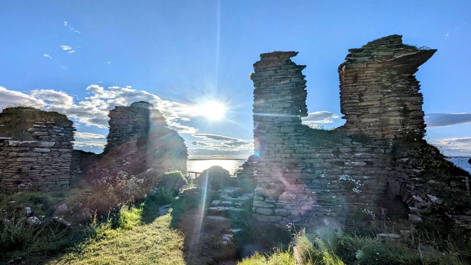 Inside the ruined walls of Castle Sinclair Girnigoe with the low evening sun bursting between two broken stone gables and the sea beyond.