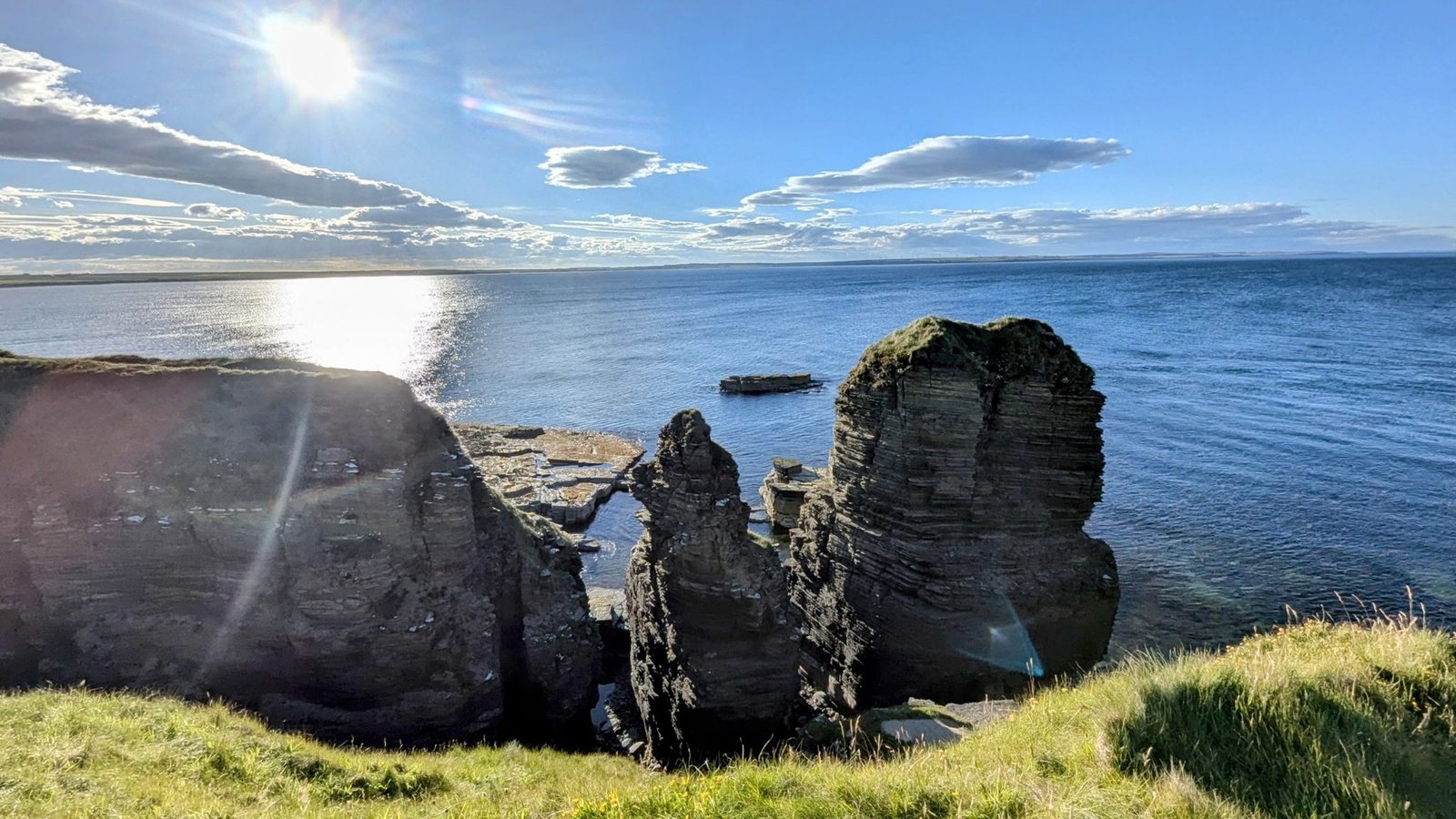 Layered flagstone sea stacks and cliffs at Noss Head near Castle Sinclair Girnigoe, blue sea and low sun.