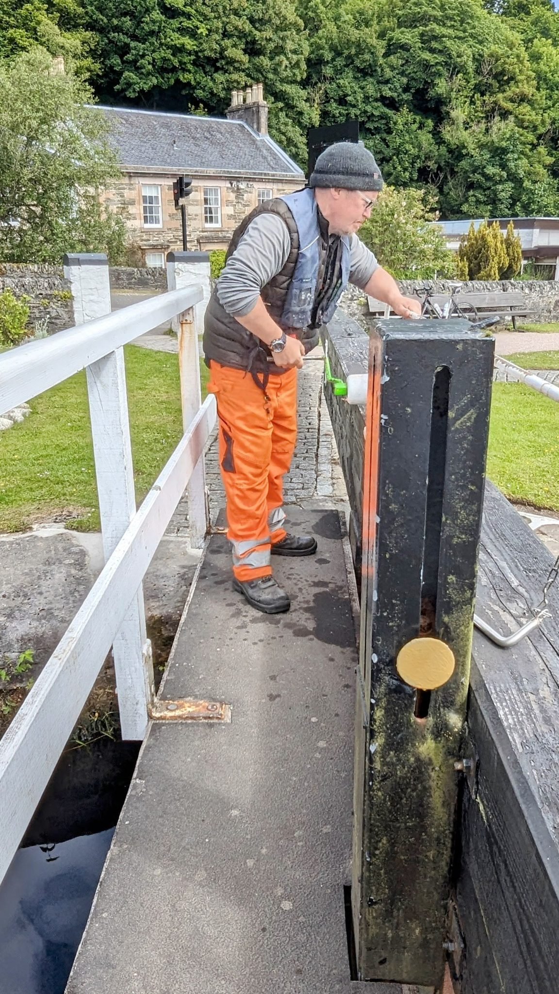 A lock-keeper in orange overalls operating a lock gate on the Crinan Canal.