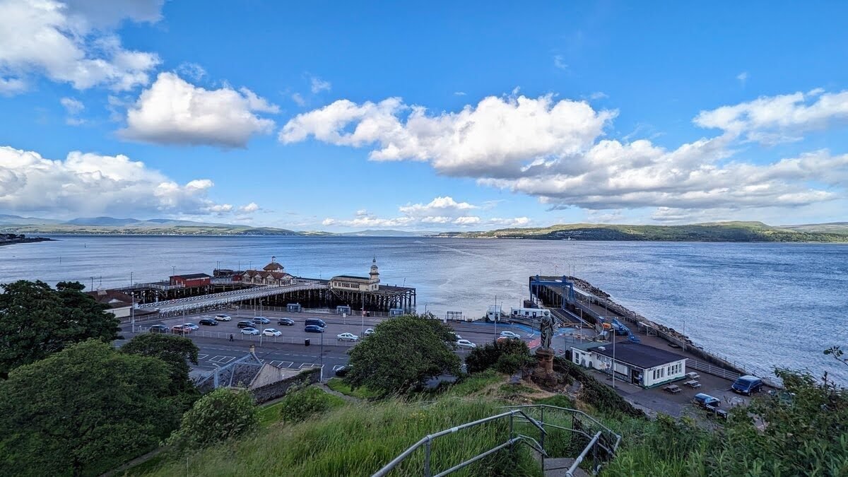 Dunoon's Victorian pier, ferry terminal and seafront town seen from above, the Firth of Clyde and hills beyond.