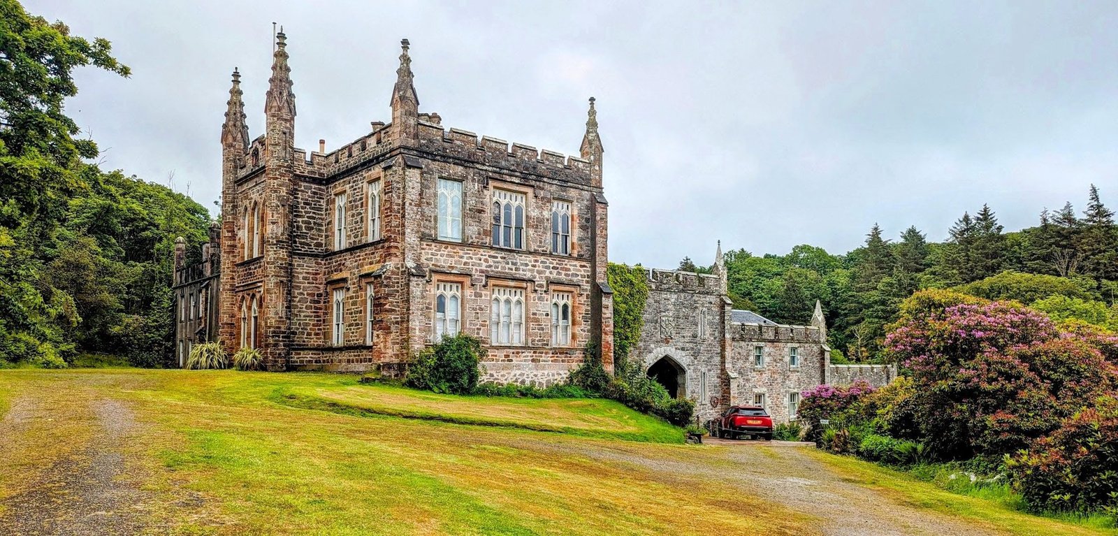 The castellated Gothic-Revival frontage of Glenbarr Abbey in Kintyre, with pinnacles, pointed windows, a gatehouse arch and rhododendrons.