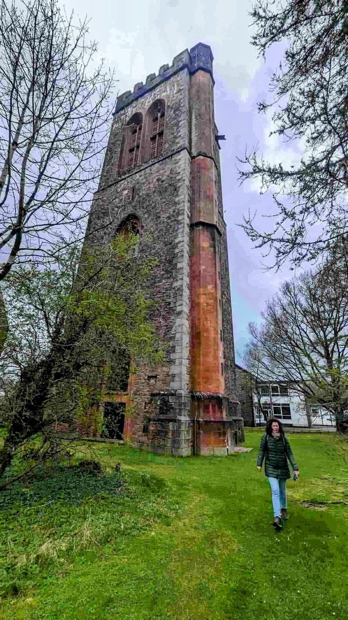 The tall red-and-grey stone Inveraray Bell Tower rising above trees, a figure at its base for scale.