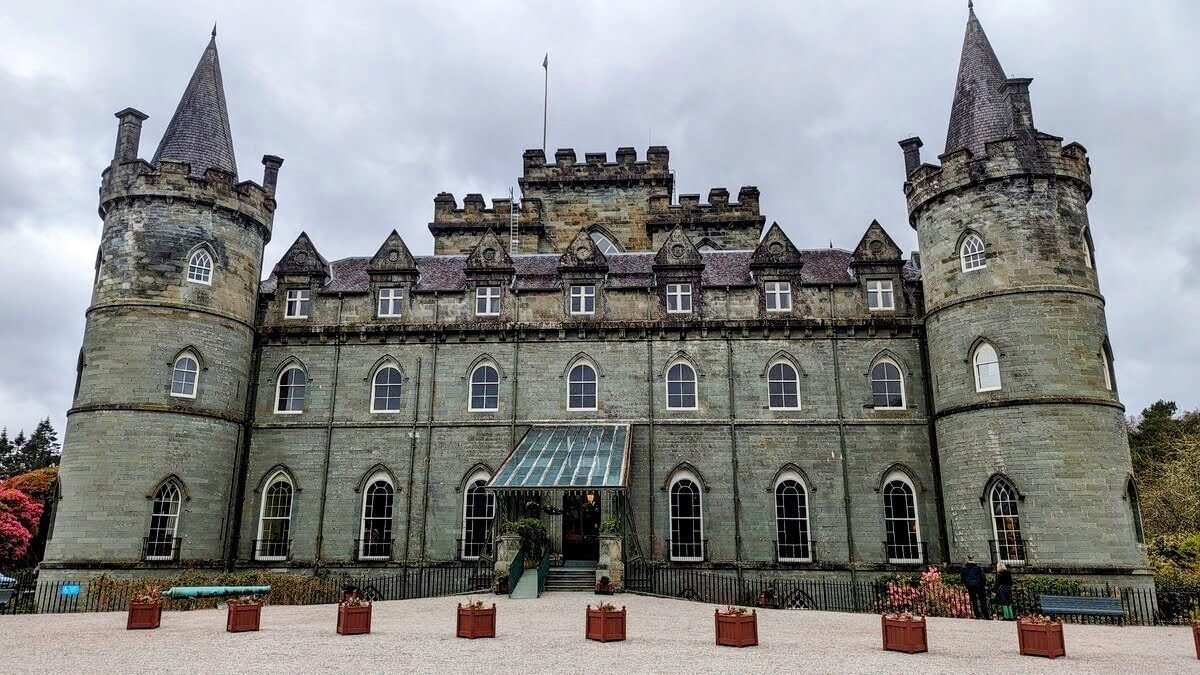 Inveraray Castle — a grey Gothic-Revival castle with conical-roofed corner turrets — seen across its lawn under a moody Argyll sky.