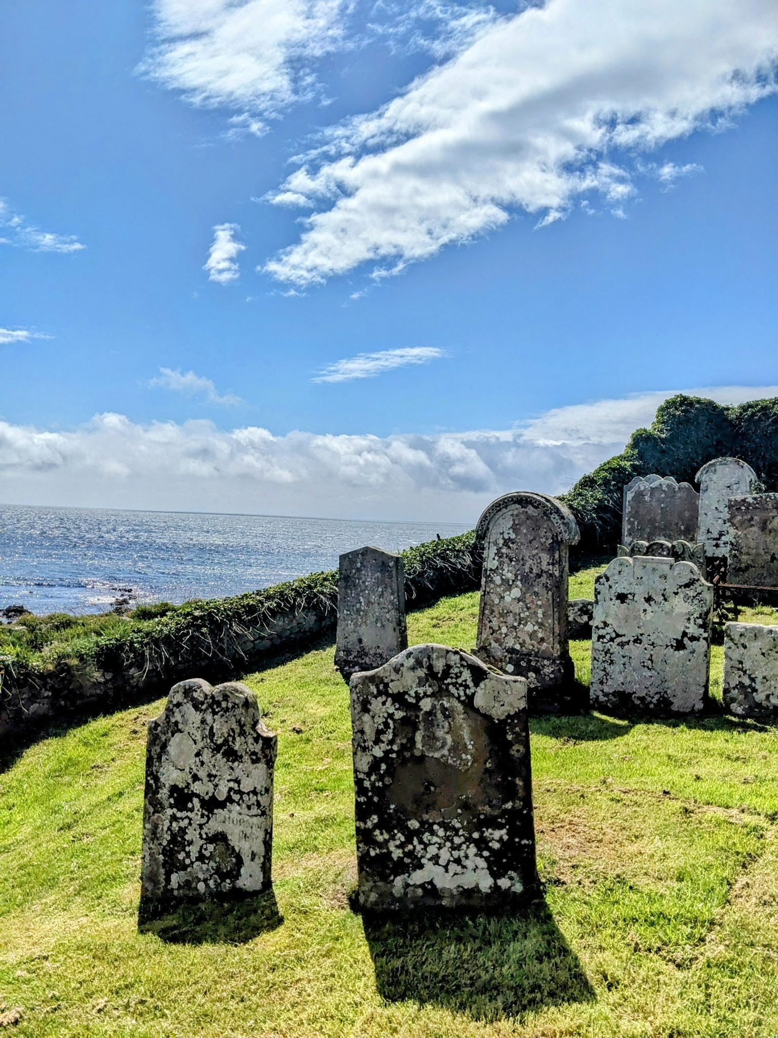 Ancient upright gravestones in the ruined graveyard at Keil, with the sea beyond.