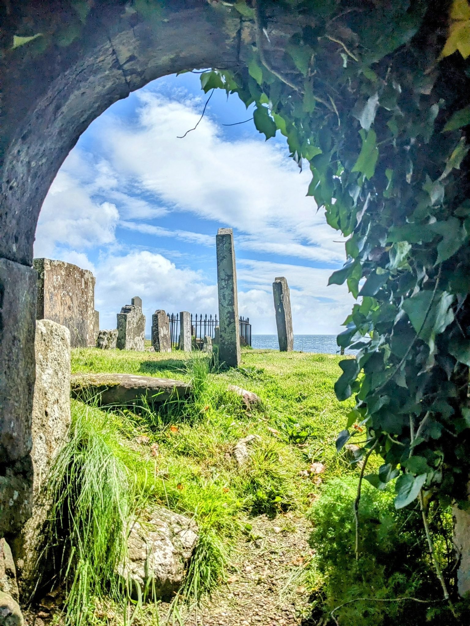 The ivy-draped ruined arch of St Columba's Chapel at Keil, framing ancient standing gravestones and the sea beyond.