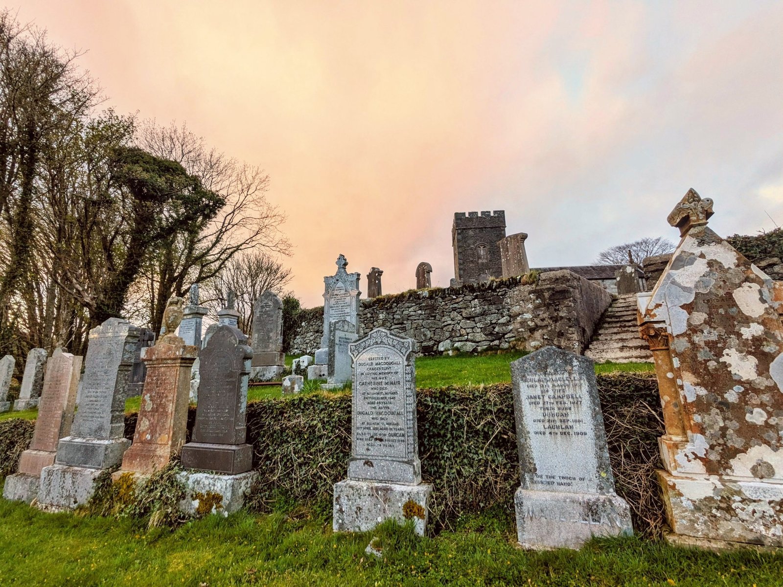 Old gravestones and the church tower in Kilmartin churchyard under a warm sunset sky.