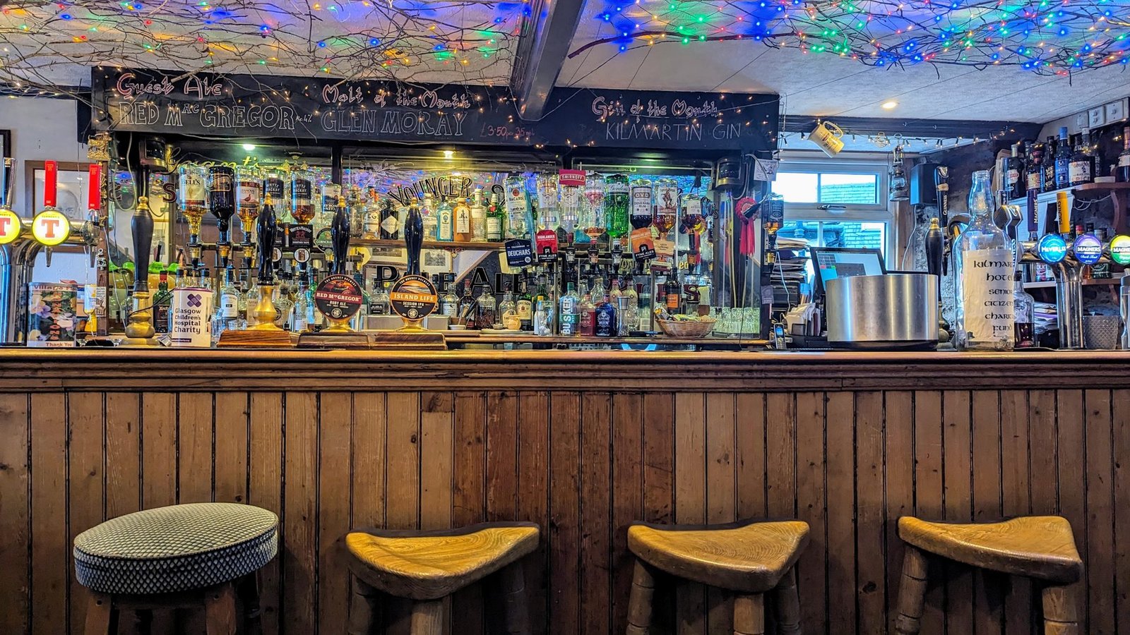The warm wooden bar of the Kilmartin Hotel with stools and beer taps.