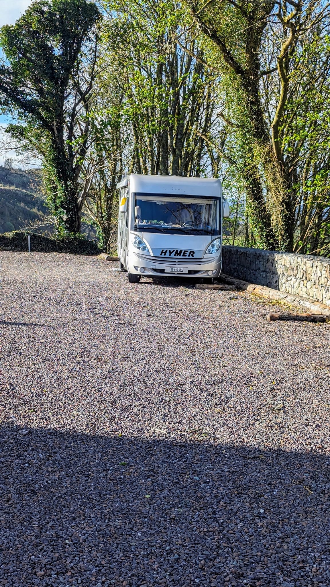 A motorhome parked on a quiet gravel area under tall trees near Kilmartin.