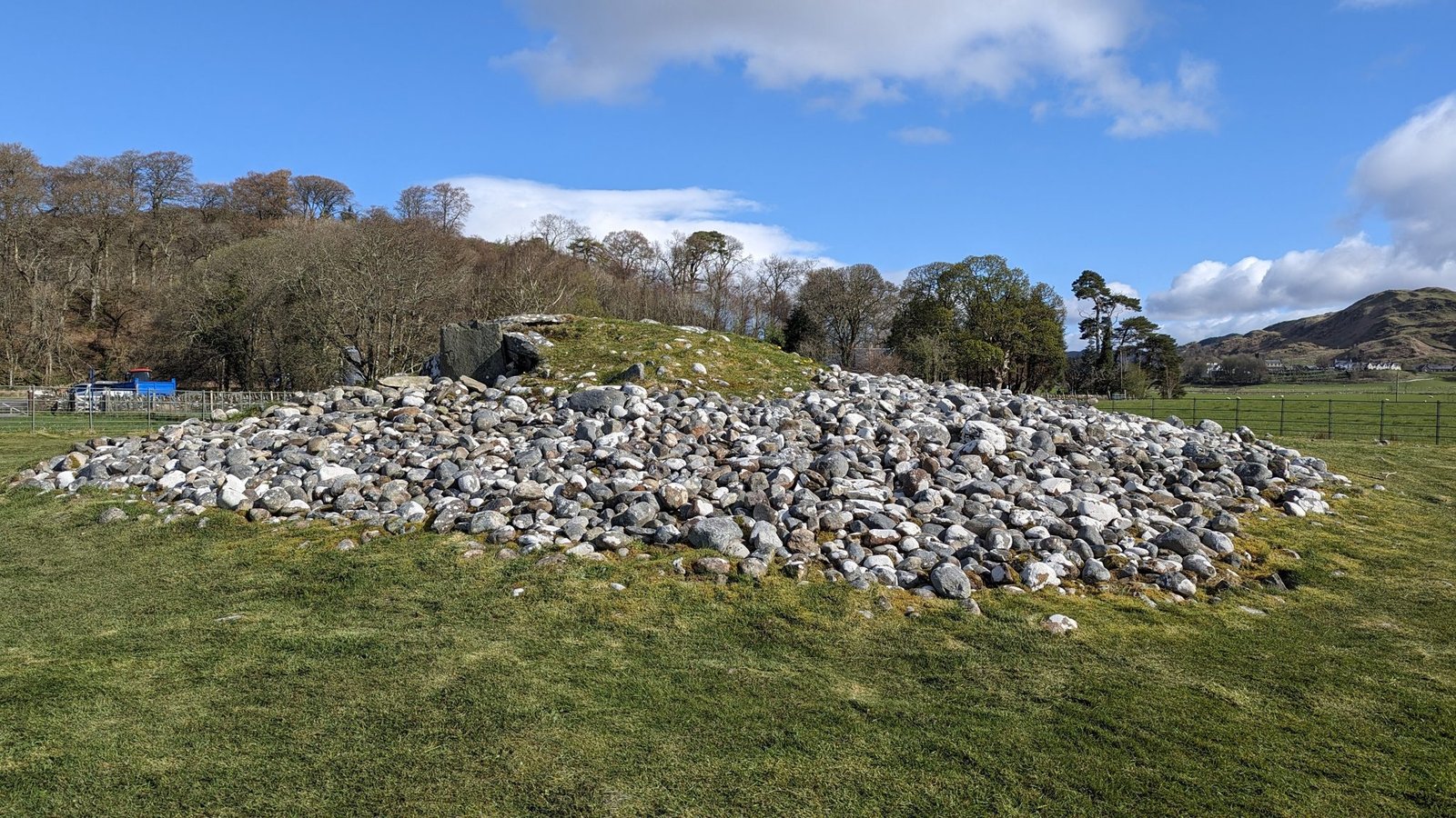 A large Bronze Age burial cairn of grey stones in a green field in Kilmartin Glen.