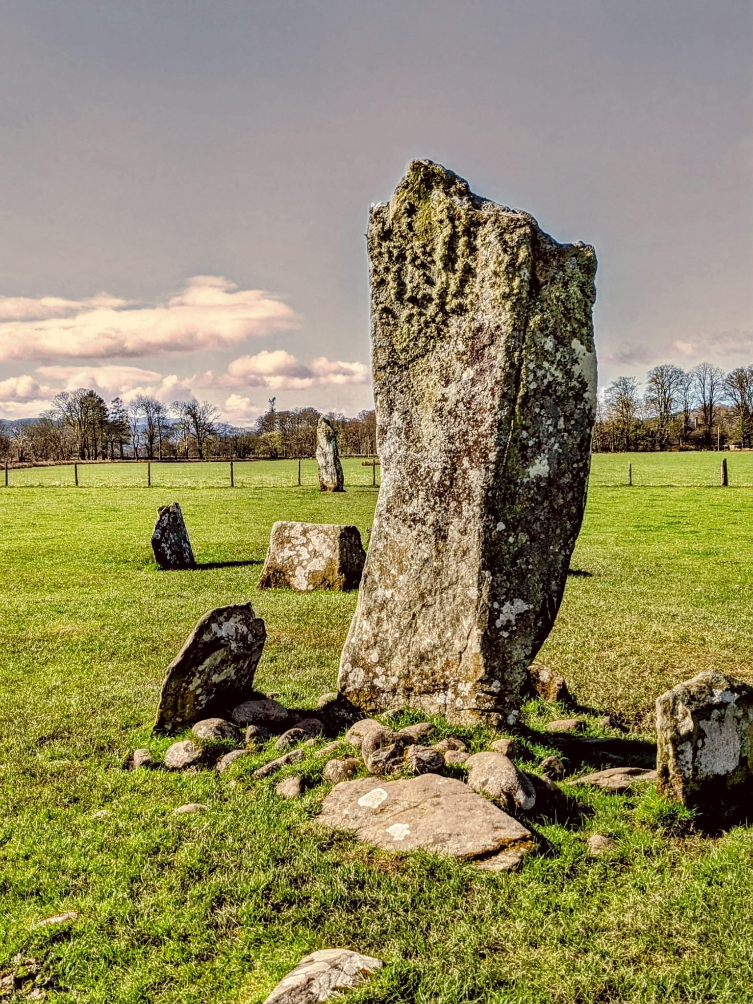 A group of tall prehistoric standing stones set in green fields at Nether Largie, Kilmartin Glen, hills behind.