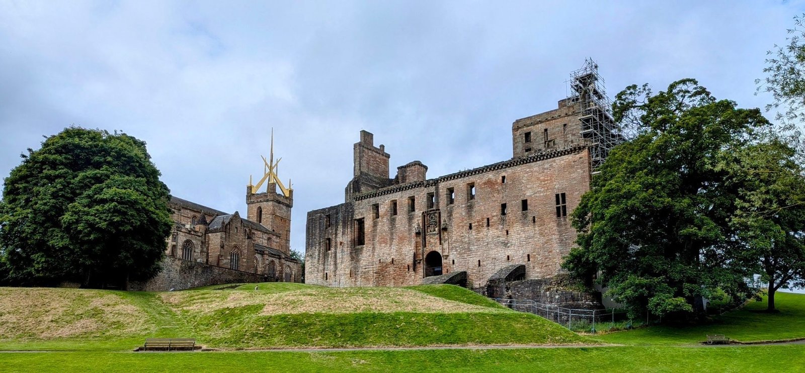 Linlithgow Palace and the crown-spired St Michael's Church standing together on a green mound above Linlithgow Loch.