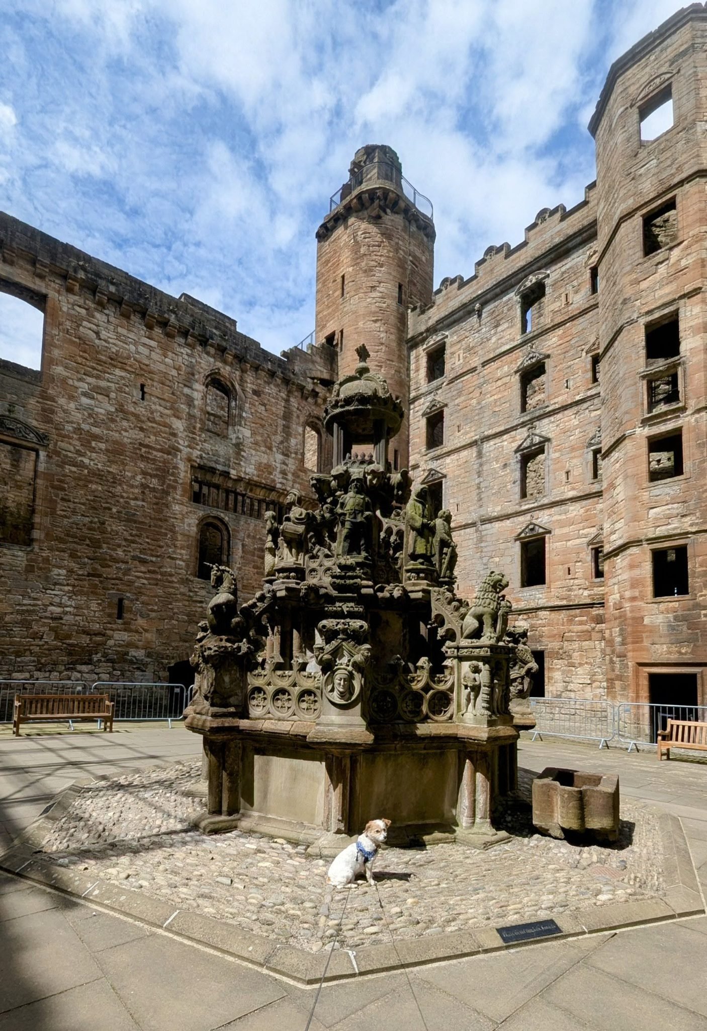 The ornately carved stone King's Fountain in the courtyard of ruined Linlithgow Palace, with the palace tower behind.