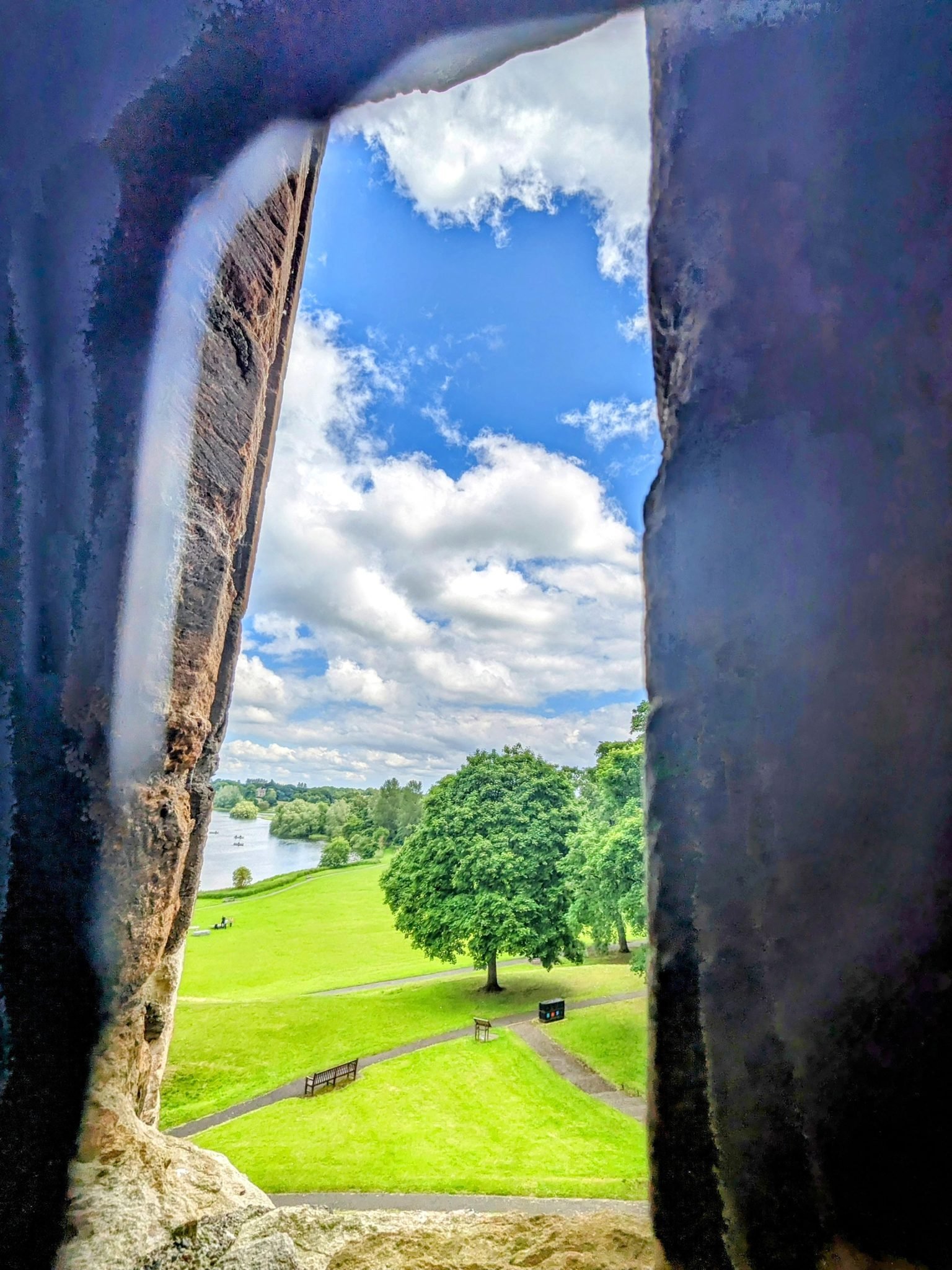 A view out through a stone window of Linlithgow Palace over the trees to Linlithgow Loch.