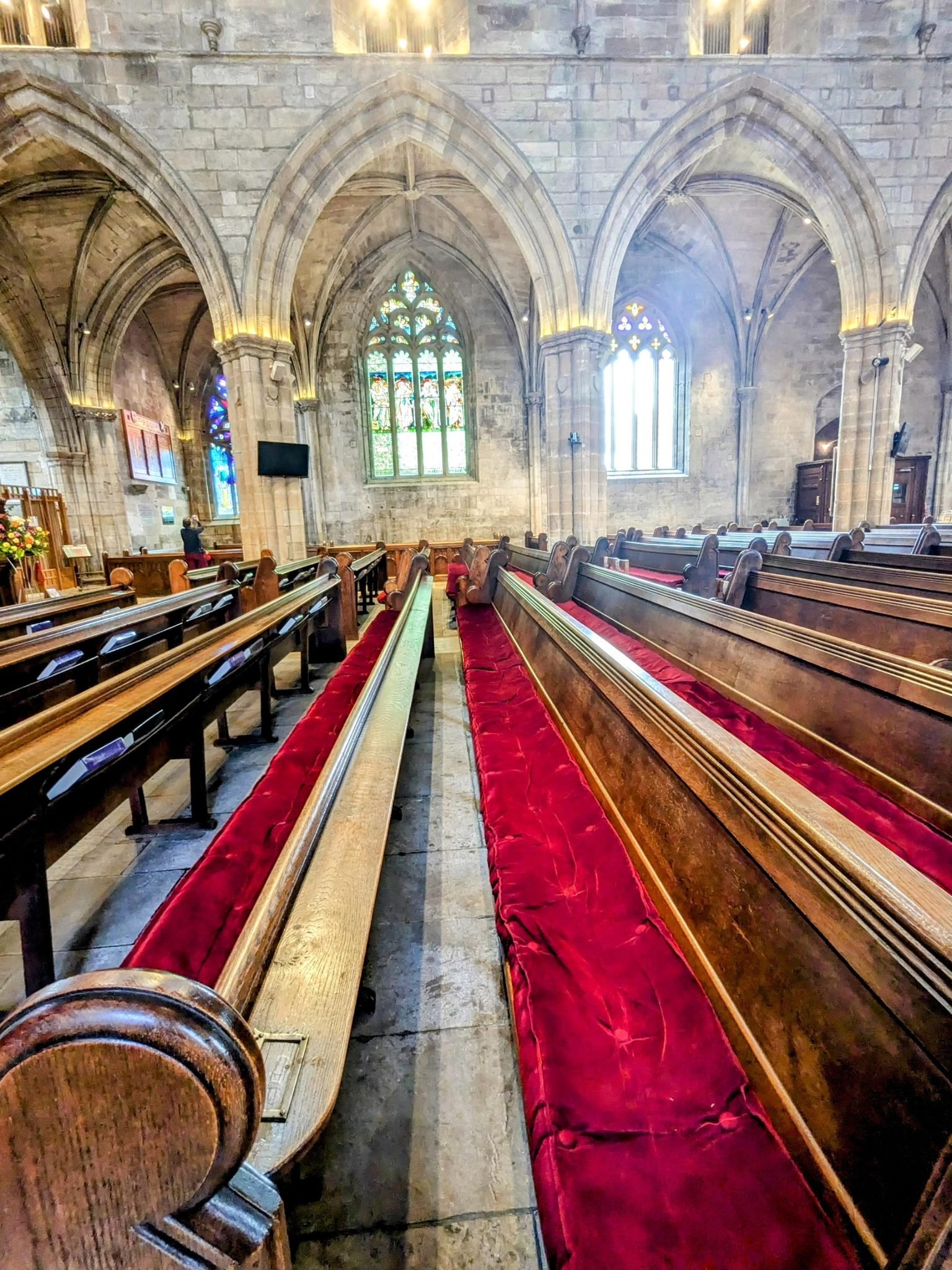 The Gothic nave of St Michael's Church, Linlithgow, with wooden pews, a red carpet and a stained-glass window.