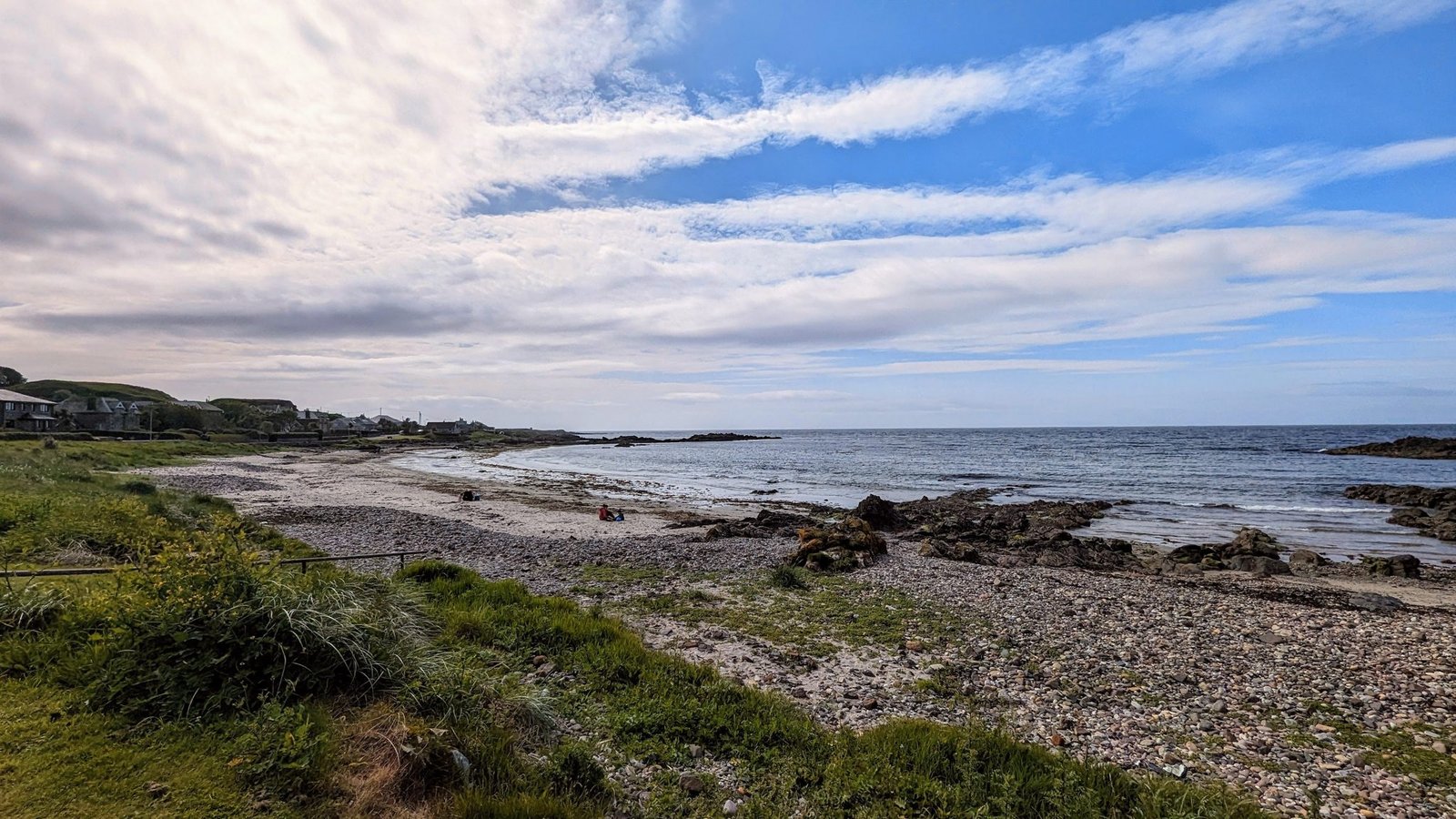 A wide panorama of Machrihanish Bay — a long rocky and sandy Atlantic shore under a big sky, village houses to one side.