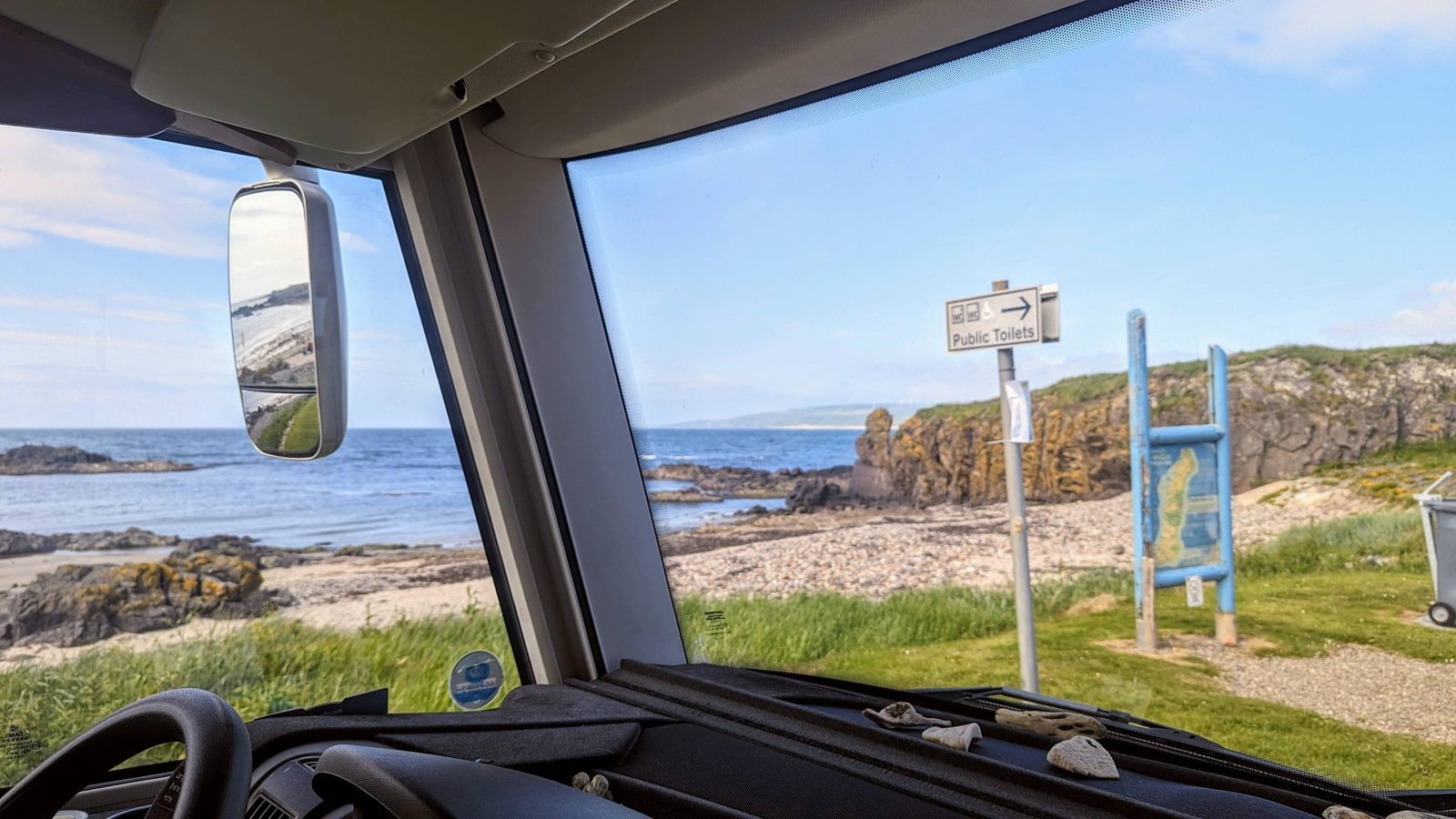 The view out of a motorhome windscreen at Machrihanish, looking across the rocky beach to the sea and a signpost.