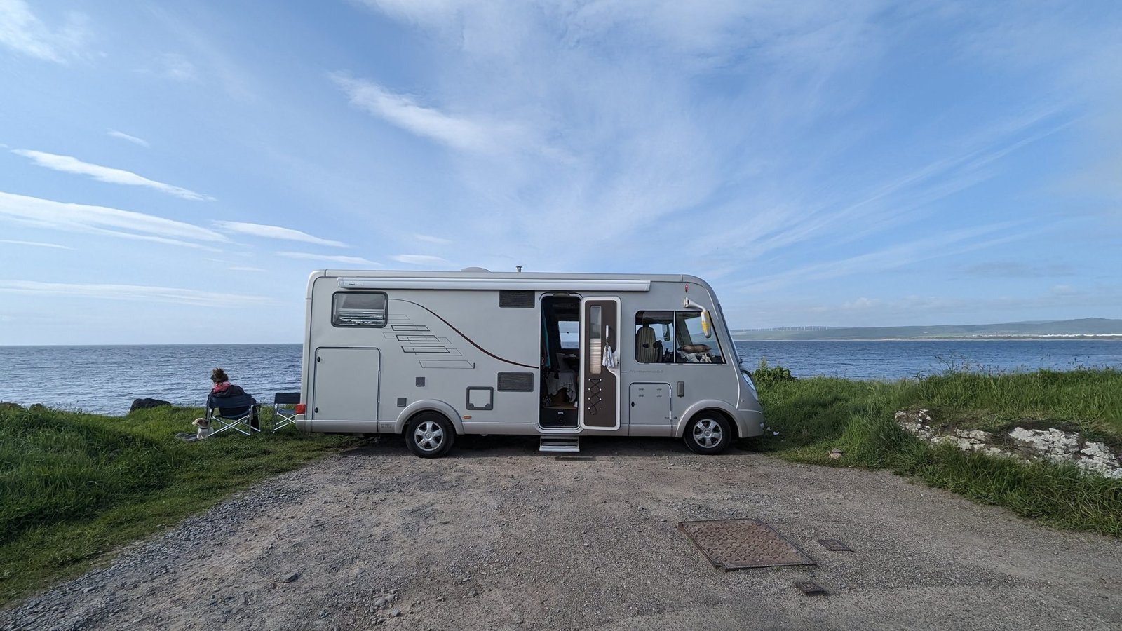A motorhome parked by the shore at Machrihanish in the evening, a person sitting on a chair looking out over the Atlantic.