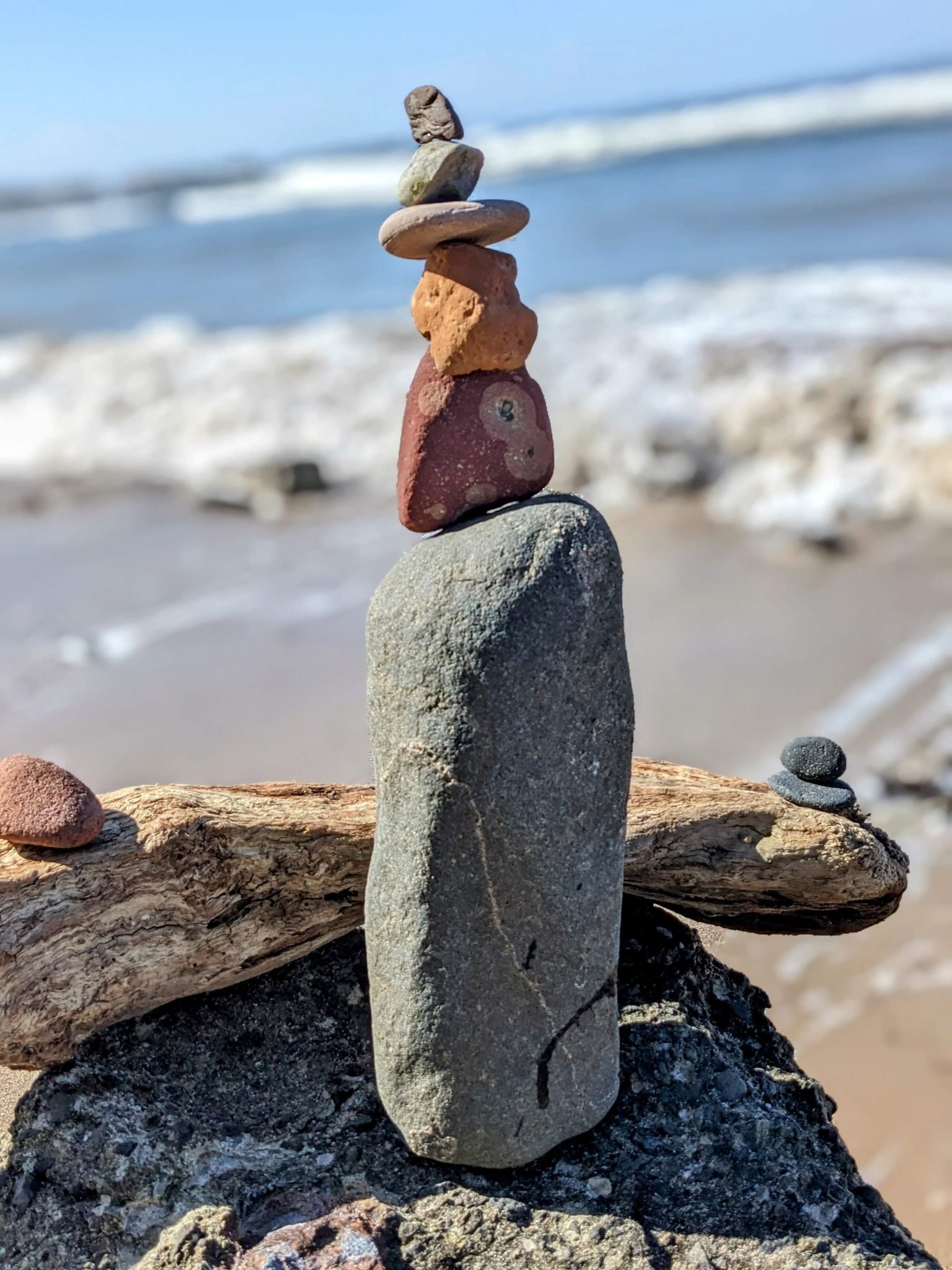 A balanced stack of coloured beach pebbles on driftwood on a North Berwick beach, sea behind.