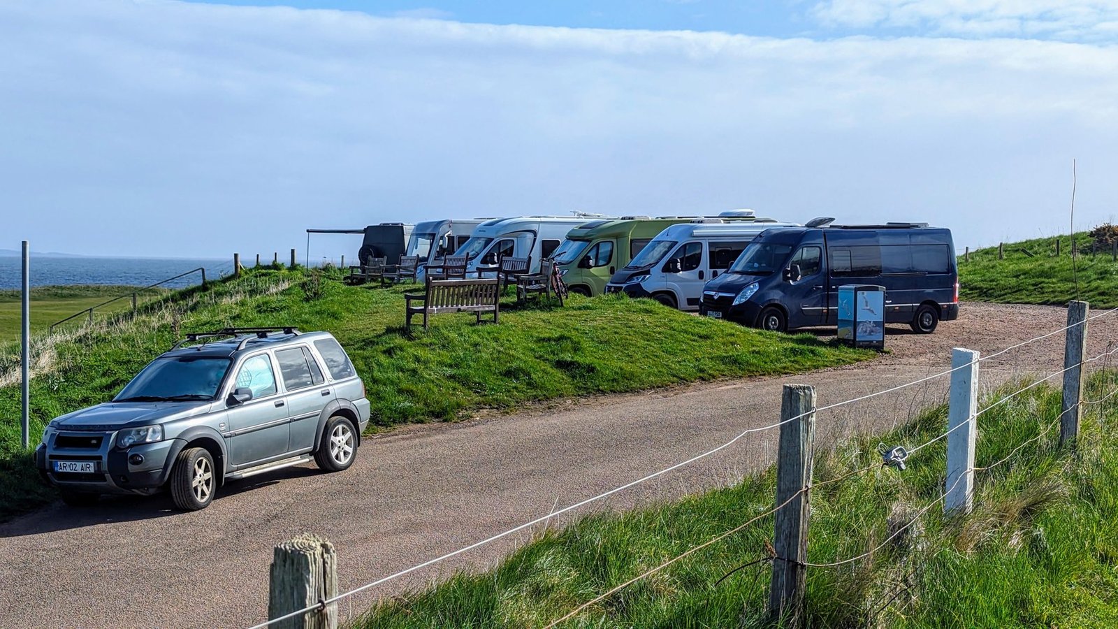 Motorhomes and campervans on a grassy clifftop above the sea near North Berwick in soft light.