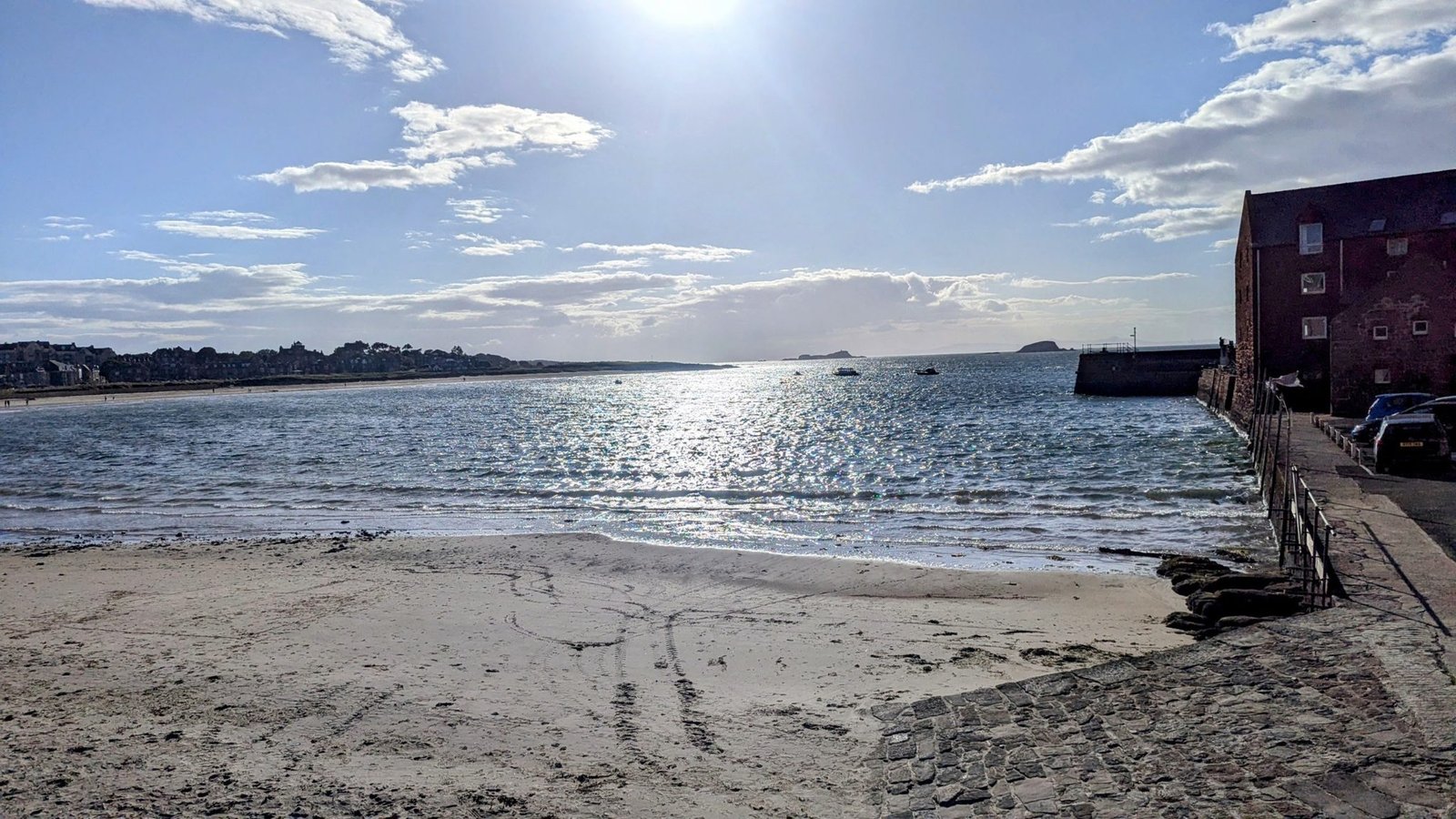 North Berwick harbour and West Bay beach curving toward the town in golden light, the red-sandstone Scottish Seabird Centre on the right and islands on the horizon.