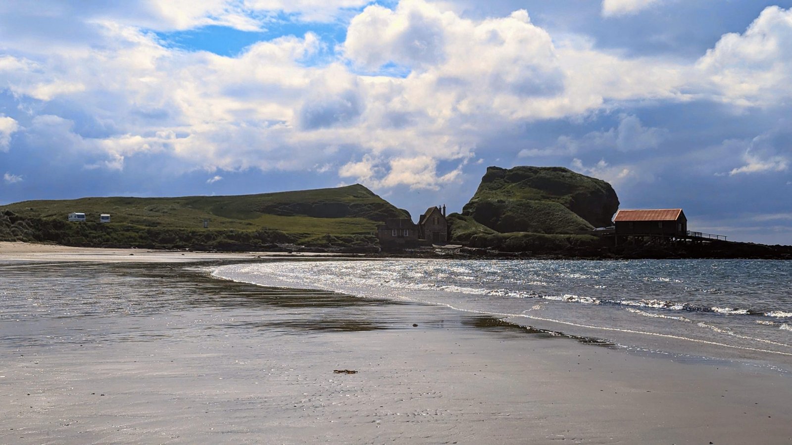 The wide sandy beach at Southend, Kintyre, with a rock stack and lifeboat-style building across the sand at low tide.