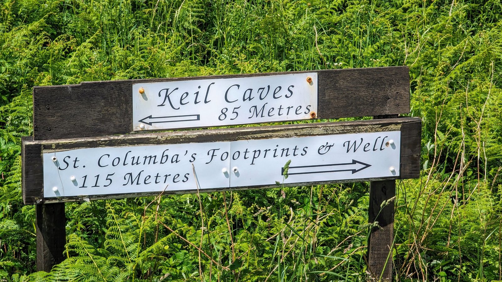 A wooden signpost pointing to Keil Caves and St Columba's Footprints & Well near Southend.