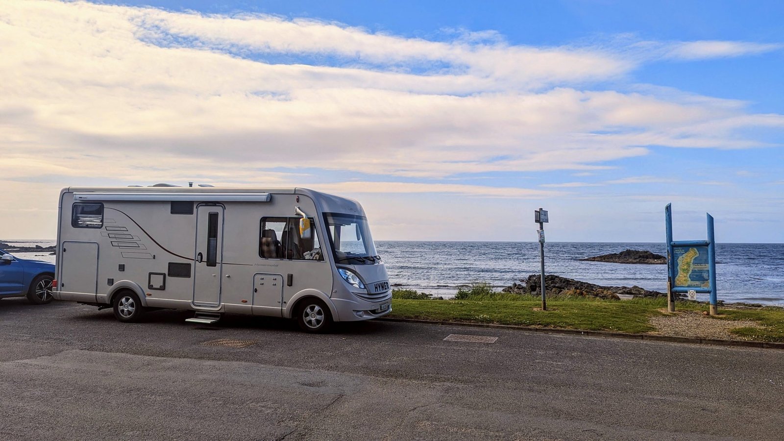A motorhome parked at a seaside car park at Southend, Kintyre, signpost and beach alongside.