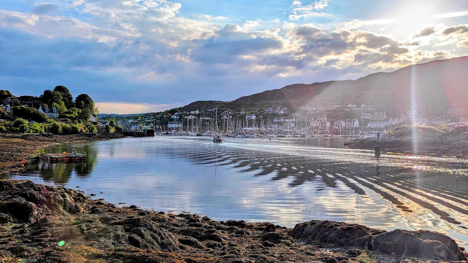 A golden sunset reflected in the calm water of Tarbert harbour, sun-rays across the loch.