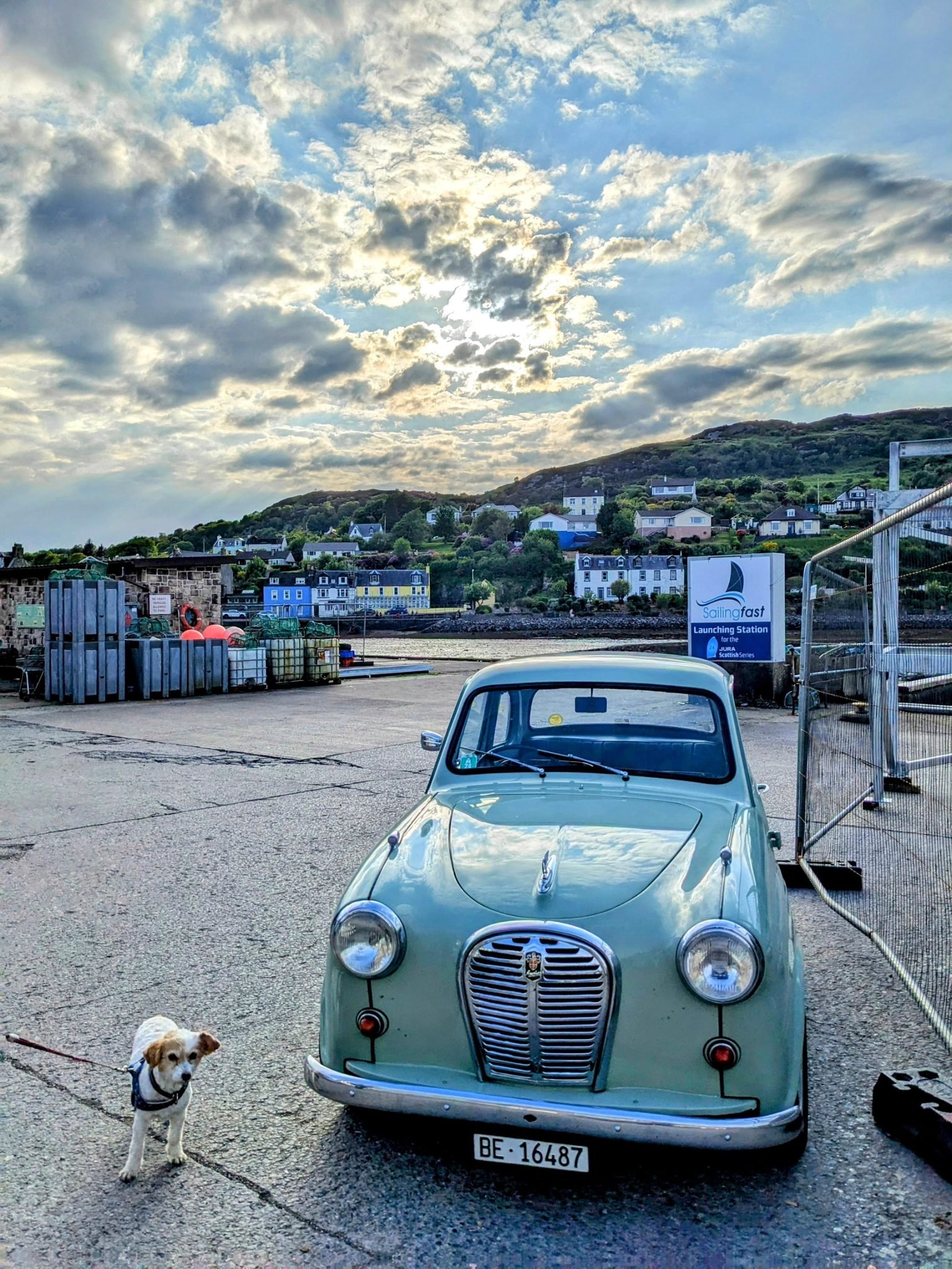 A powder-blue vintage Austin car parked on Tarbert harbour front at dusk.