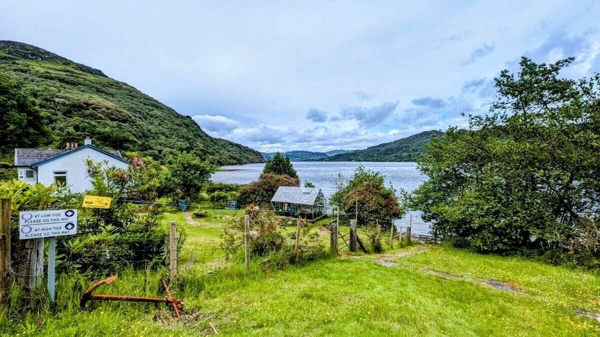 A gravel shore path near Tighnabruaich ending at a white cottage with the Kyles of Bute beyond.