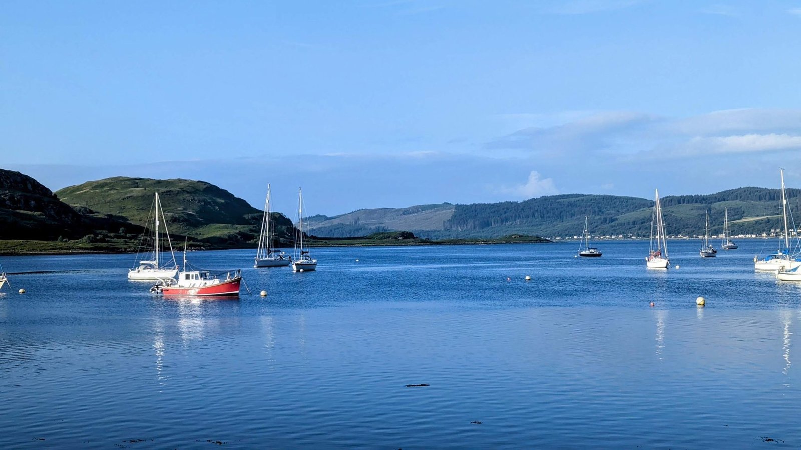 Yachts moored on the calm blue water of the Kyles of Bute off Tighnabruaich on a clear morning.